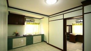 A room with a kitchenette, a window with curtains, and a door leading to another room.