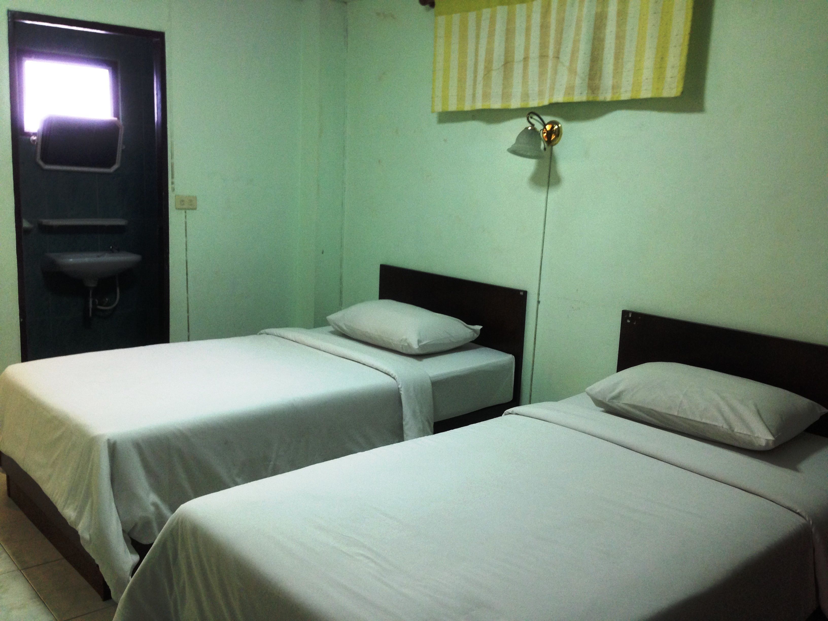 A room with two single beds, a small sink, and a window with a striped curtain.