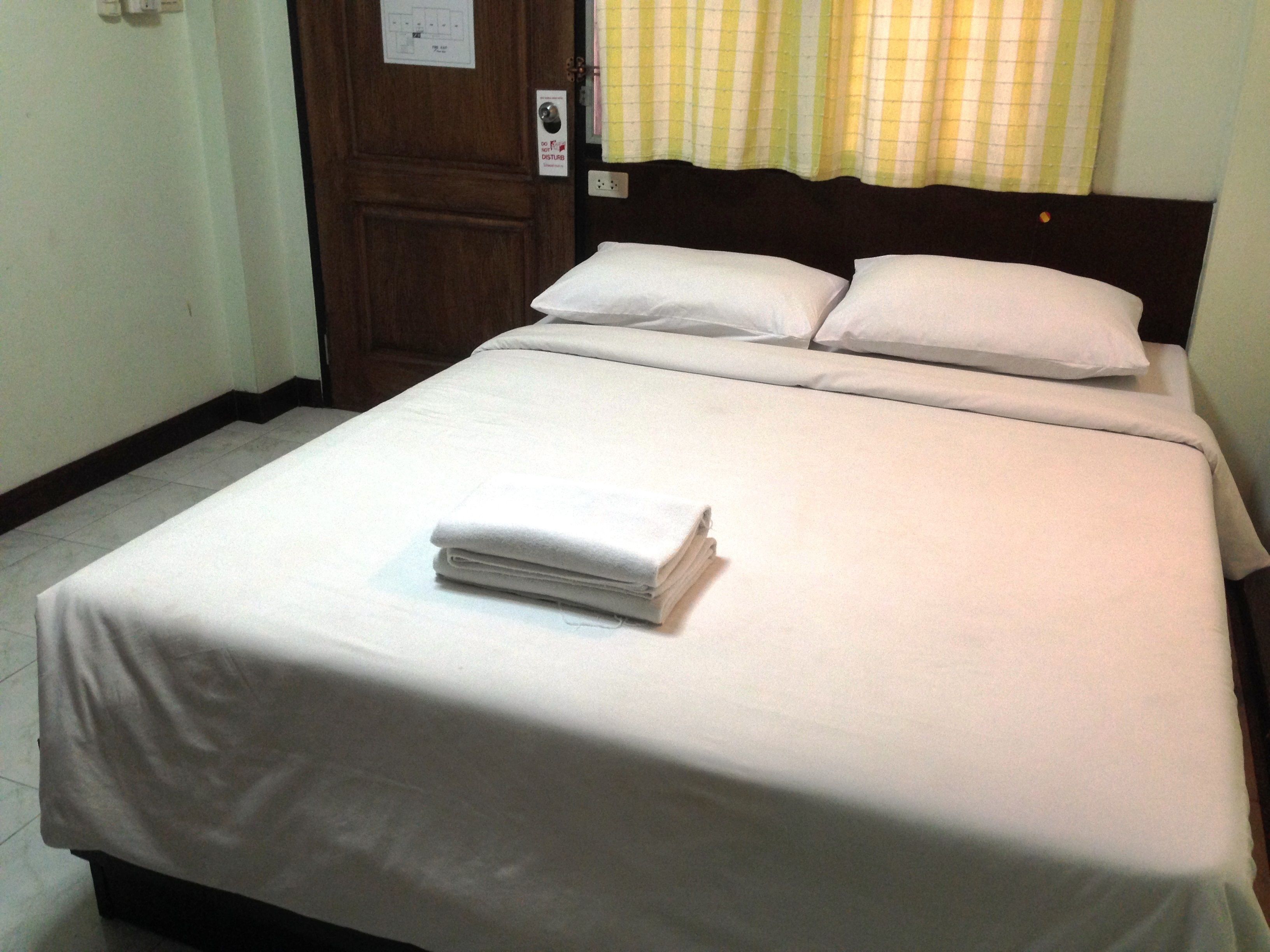 A neatly made bed with white linens and a folded towel on top, a wooden headboard, and a door with a lock and a sign indicating a do not disturb feature.