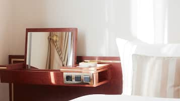 A hotel room with a wooden nightstand, a mirror, a bedside table, and a bed with white bedding.