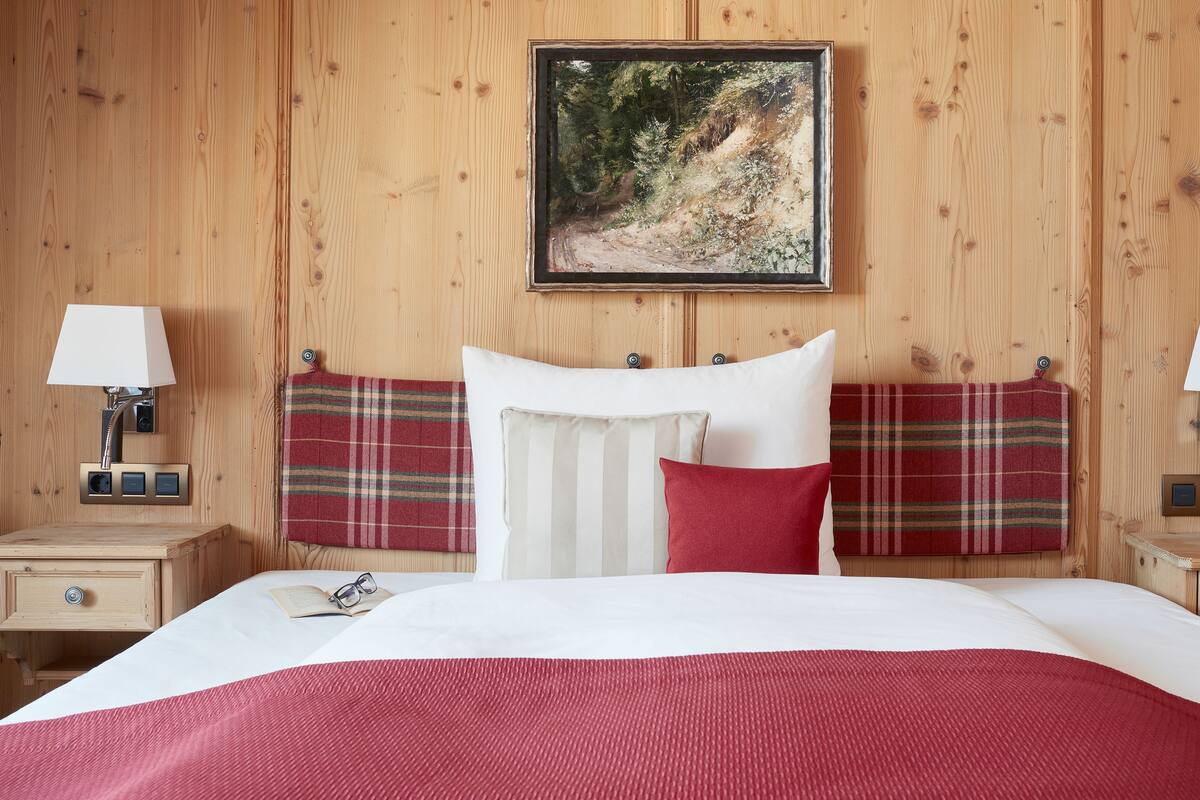 Una habitación con paneles de madera, una cama, dos mesitas de noche, un cuadro y un cabecero de cuadros rojos.