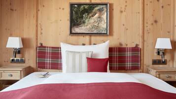 A wooden-paneled room with a bed, two bedside tables, a painting, and a red plaid headboard.