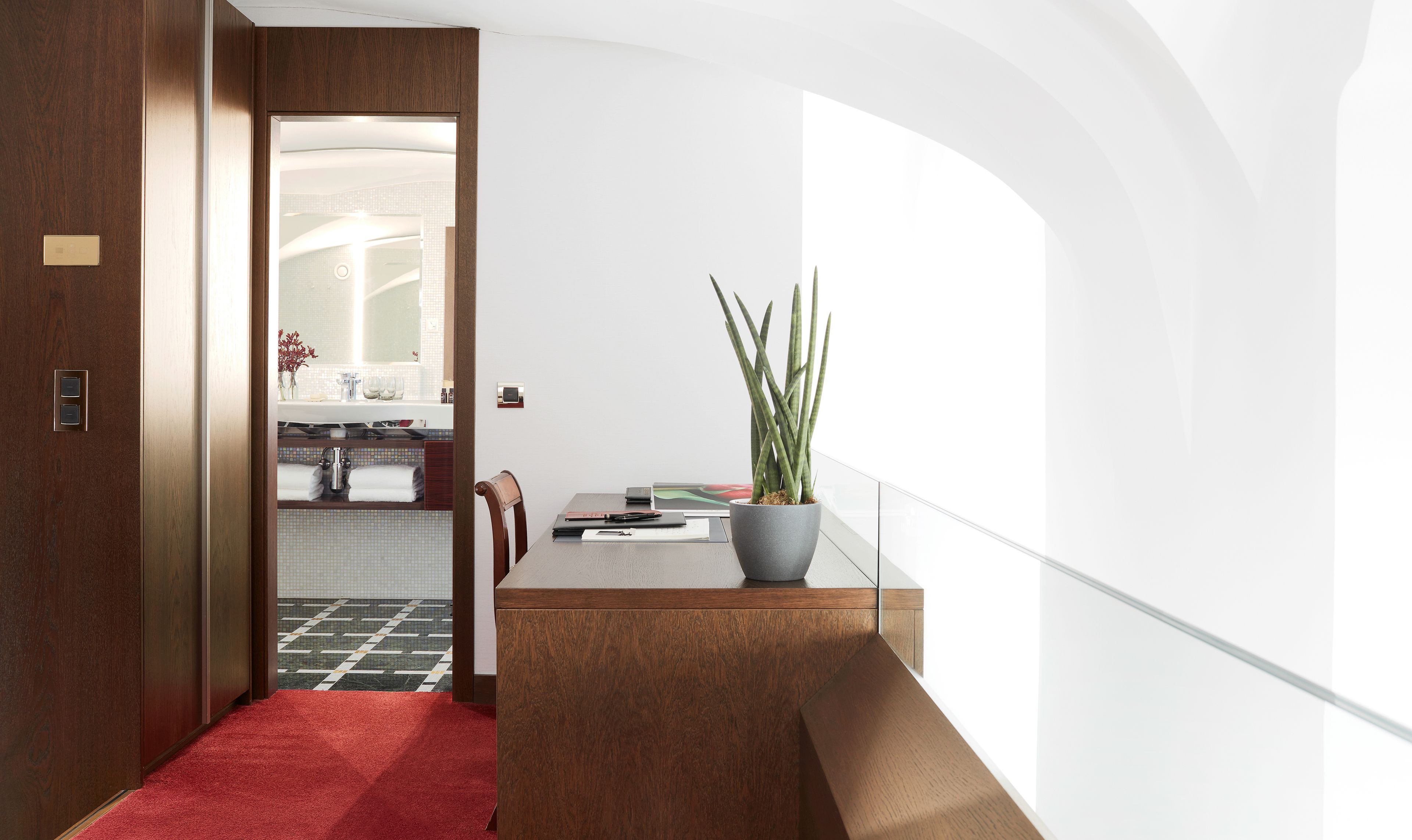 Um interior moderno com porta de madeira, corredor com carpete vermelho, área de jantar com mesa, cadeiras e planta em vaso.