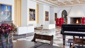 Een statige lobby met een vleugelpiano, witte banken, rode stoelen en klassieke schilderijen.