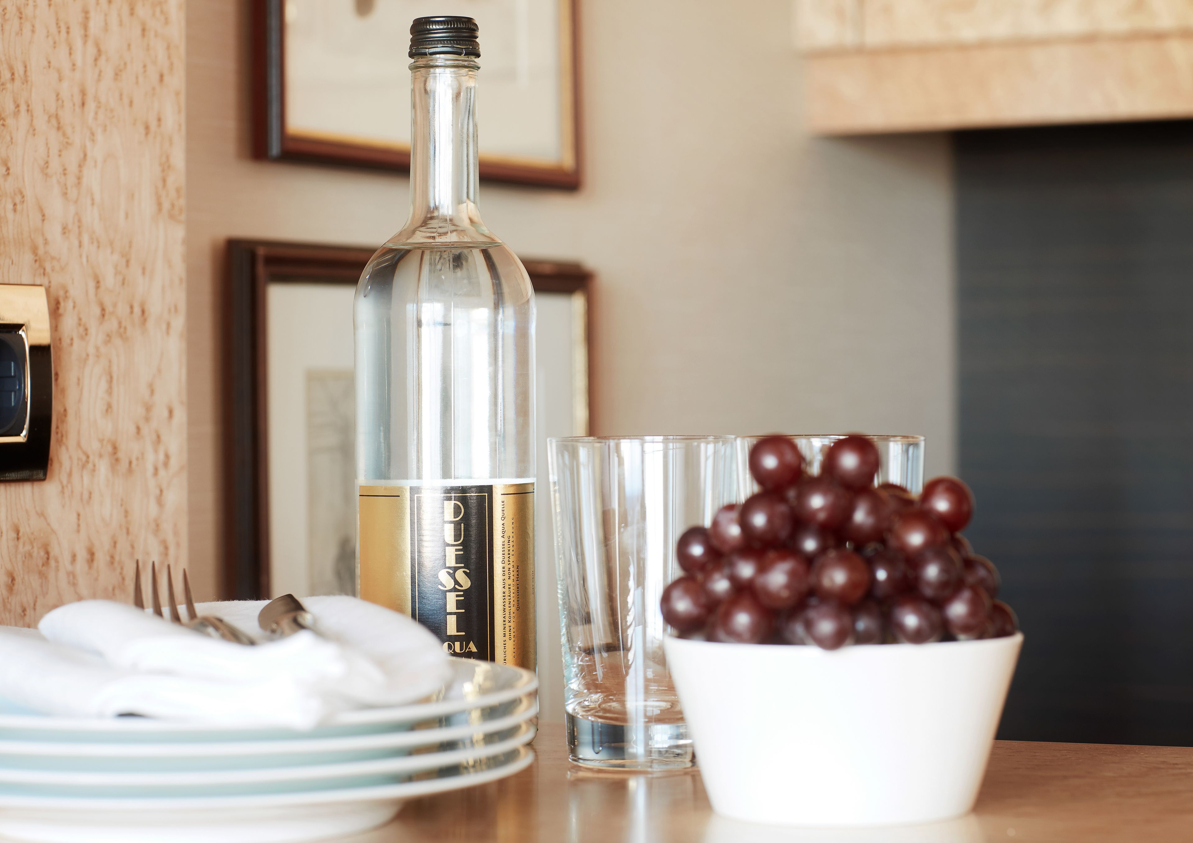 Una mesa con una botella, una copa y un cuenco de uvas.