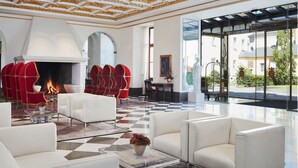 Een luxe lobby met een zwart-wit geruite vloer, rode en witte zitplaatsen, een open haard en grote ramen met uitzicht op buiten.