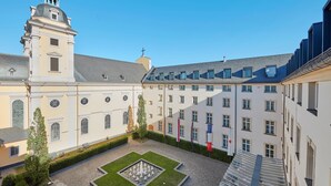 Een binnenplaats met een fontein, een kerk met een klokkentoren en aangrenzende gebouwen met veel ramen.