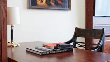 Una mesa de madera con libros, una lámpara y un cuadro en la pared.