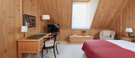 Ein Zimmer mit Holzwänden, einem Schreibtisch, einem Stuhl, einem Bett und einem Fernseher.
