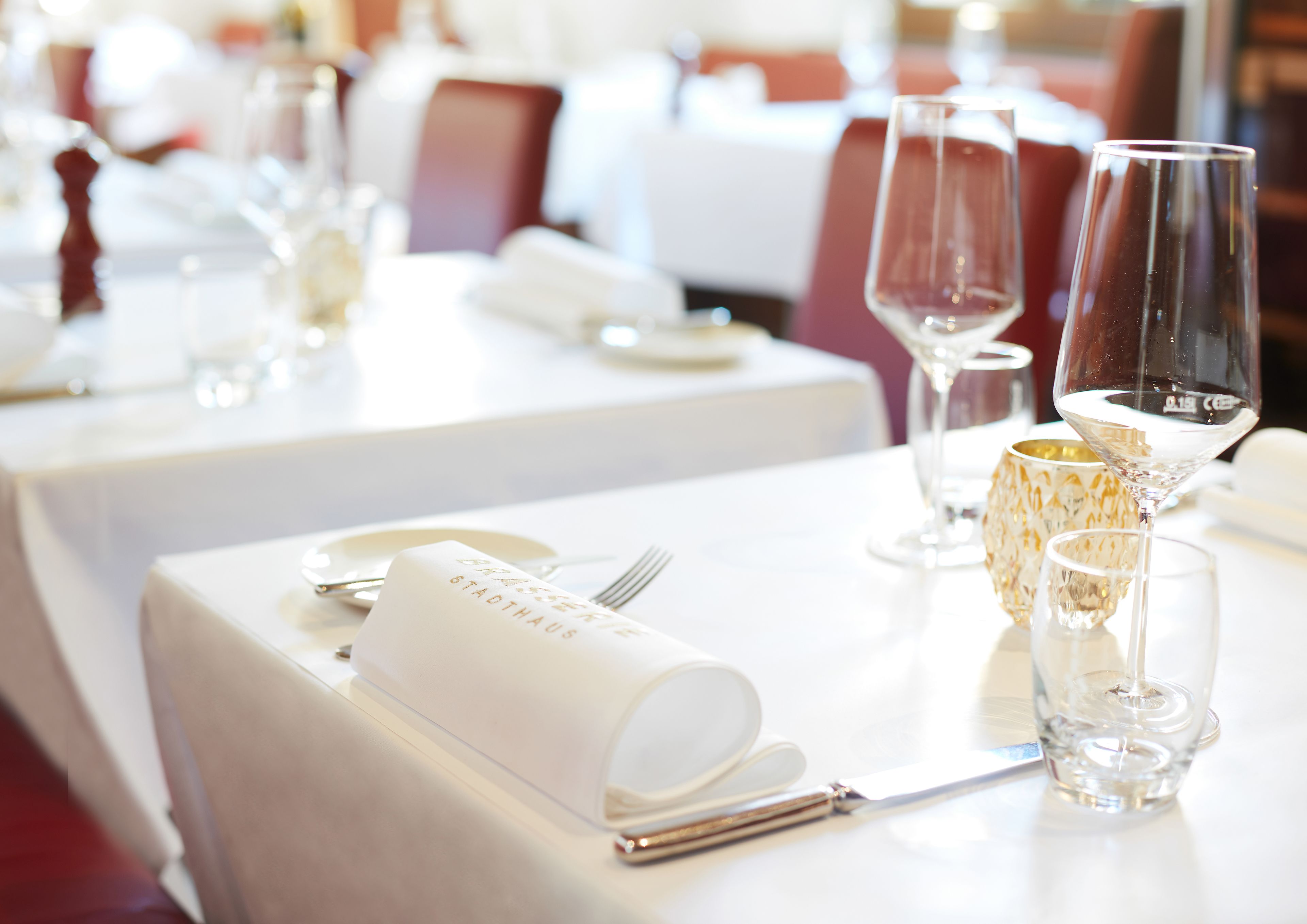 A dining table set with white tablecloths, clear wine glasses, and a menu holder.