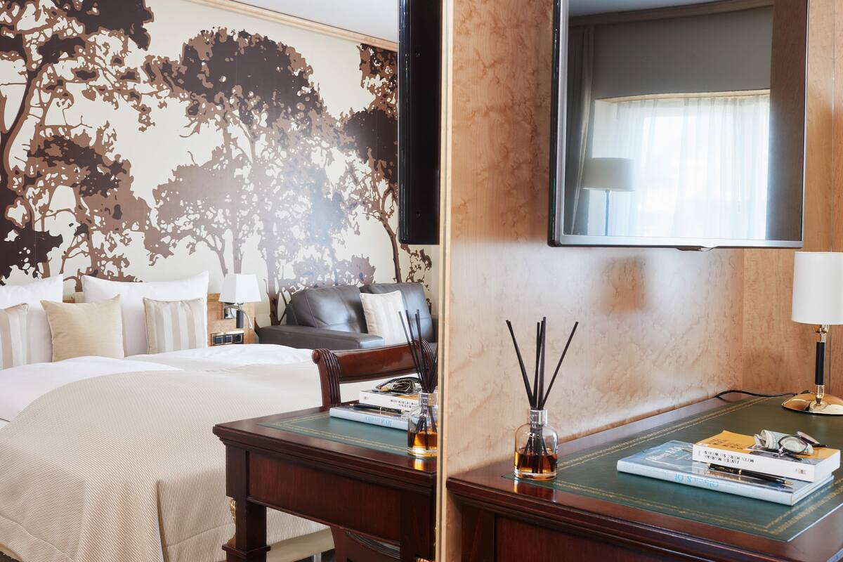 Habitación de hotel con cama, escritorio, silla, televisor y un mural de un árbol en la pared.