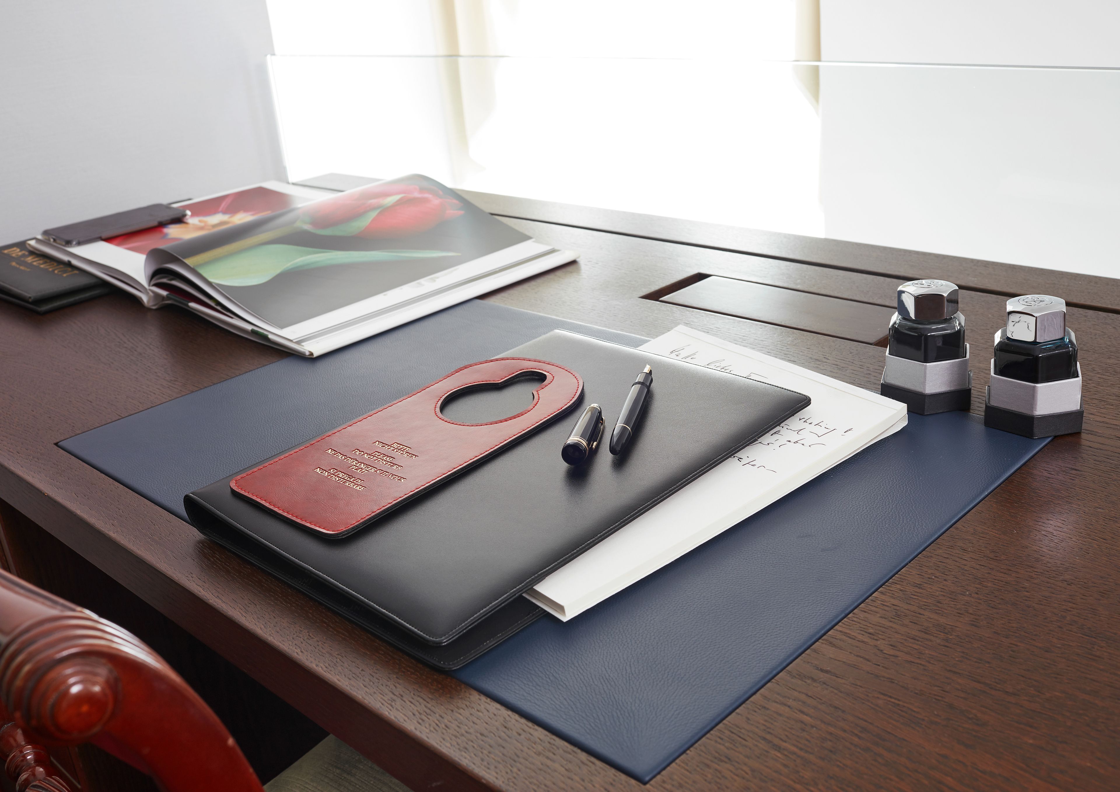 A desk with a leather case, a pen, a notebook, and two ink bottles.