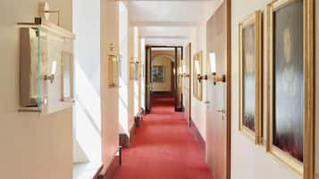 Ein Hotelgang mit rotem Teppich, gerahmten Kunstwerken und goldumrandeten Türen.