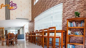 A spacious lobby with a row of wooden chairs and a bookshelf filled with books. - J'adore Lodge (Phnom Penh)
