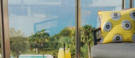 A wooden table with a view of a pool and palm trees, a yellow pillow, and a martini glass.