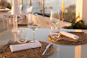 Una mesa de comedor con dos juegos de cubiertos, dos copas de vino y una servilleta doblada sobre individuales tejidos.