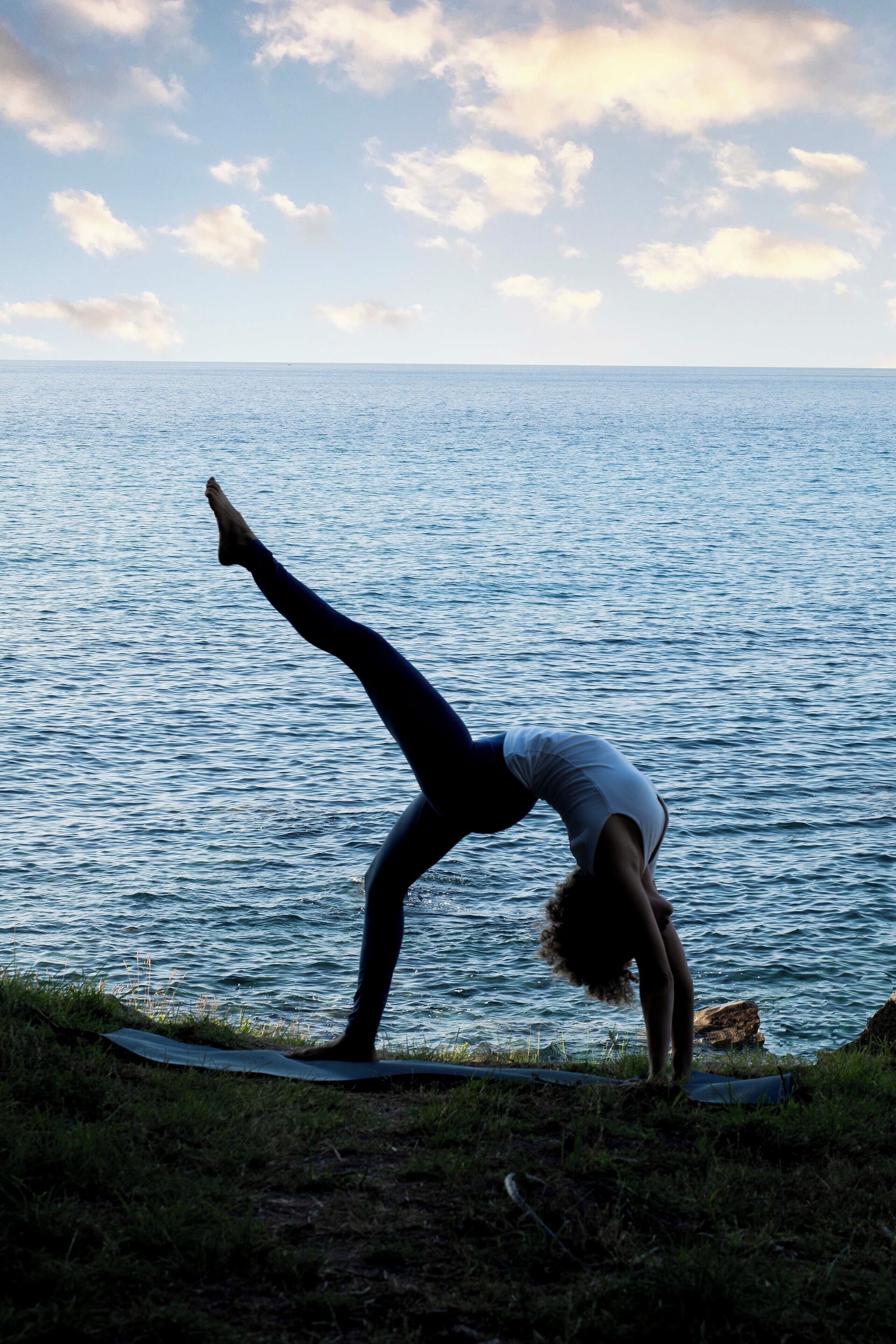 A person performing a yoga pose on a mat by the sea.