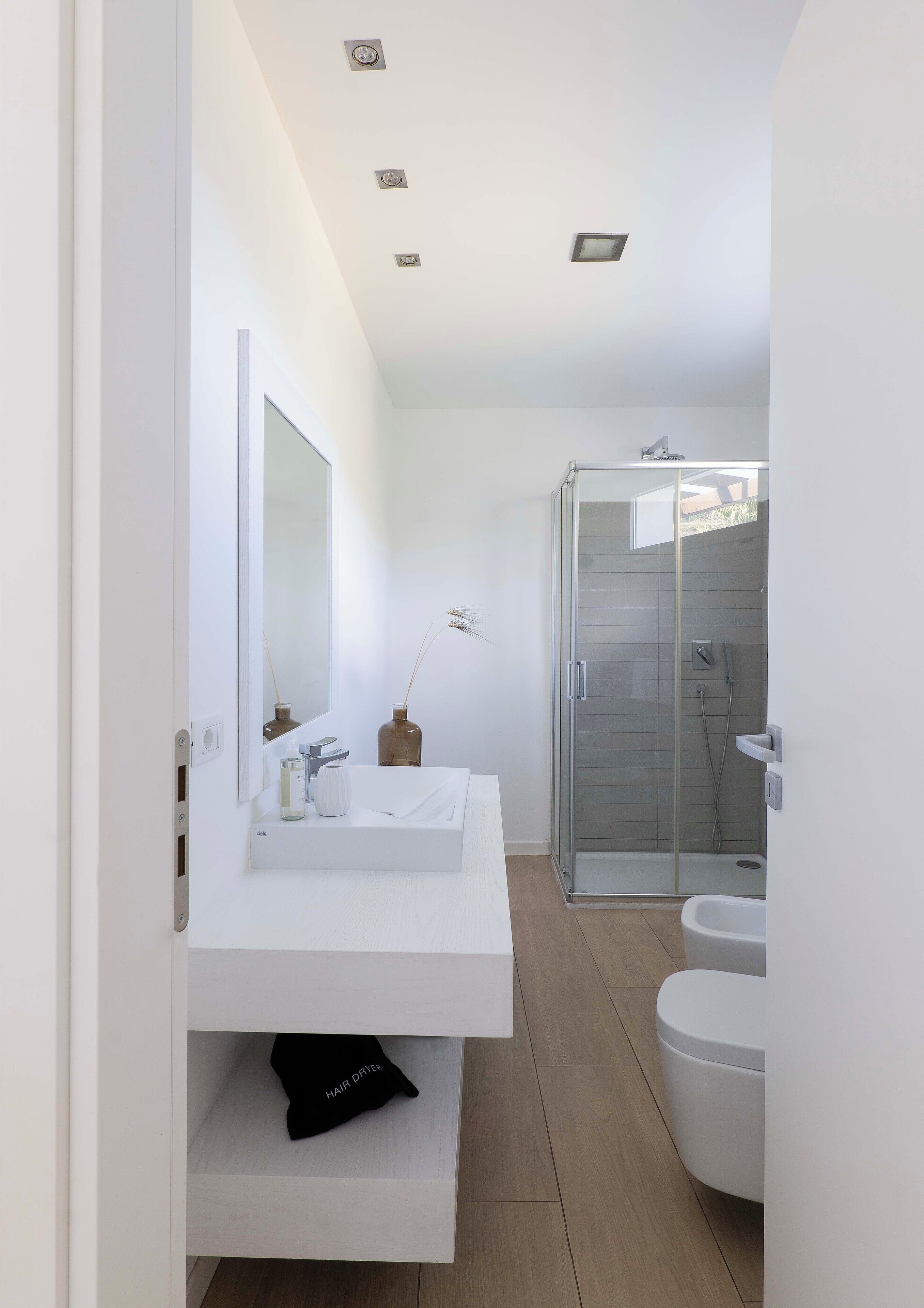 Une salle de bain moderne avec un meuble-lavabo blanc, une douche en verre et des toilettes blanches.