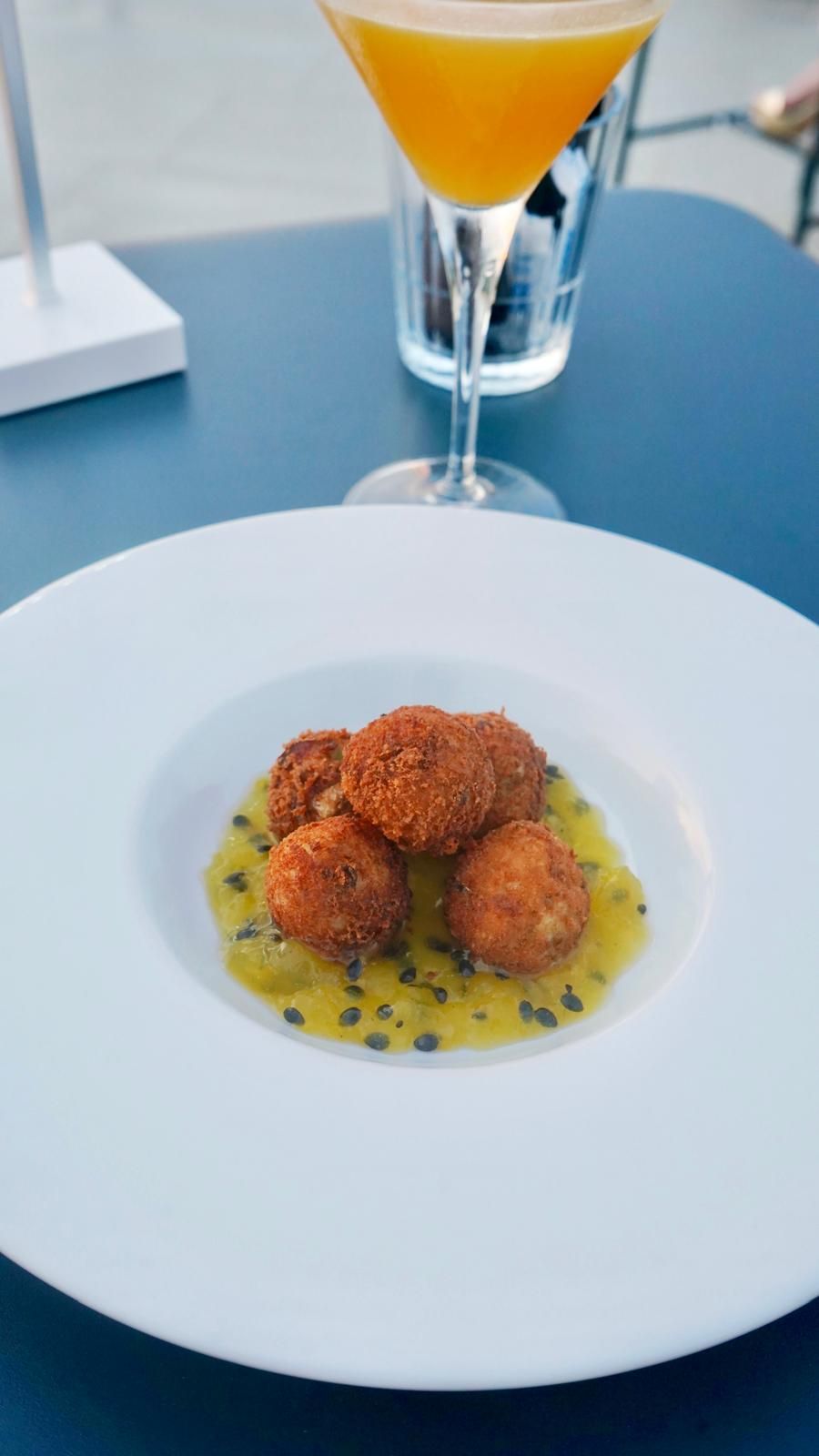 Plat de croquetes amb salsa groga i llavors negres, presentat sobre un plat blanc.