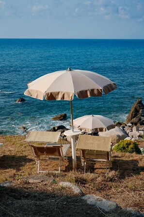 Dos sillas de playa y una sombrilla sobre una costa rocosa, con el océano al fondo.