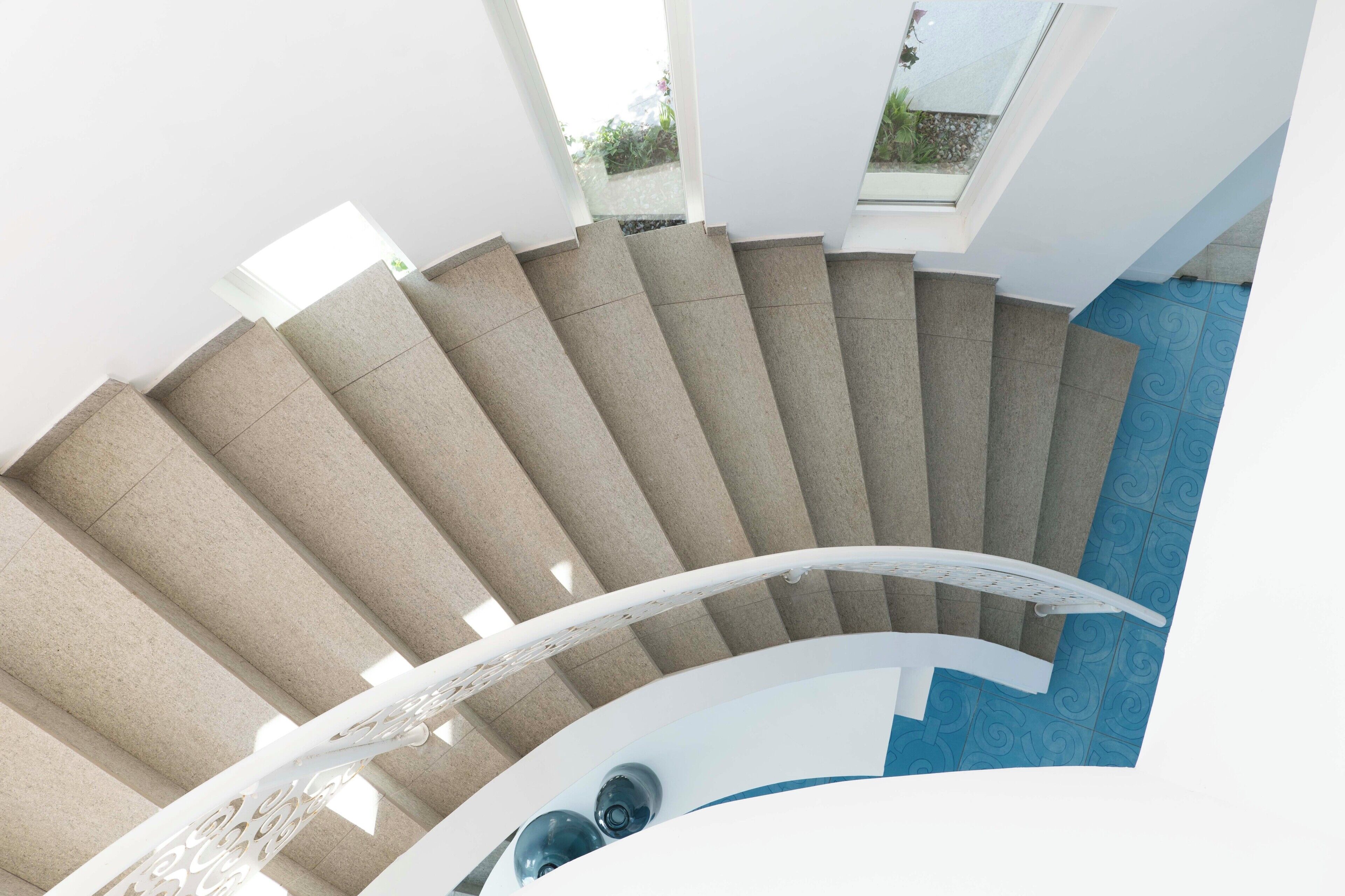 A spiral staircase with a modern design, leading to a balcony with a view of greenery.
