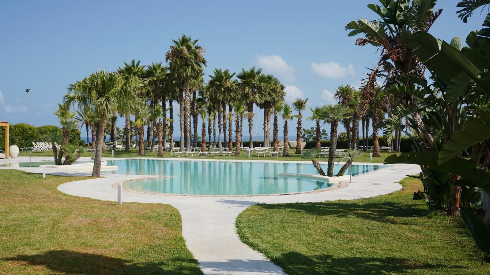 A swimming pool surrounded by palm trees and lounge chairs.