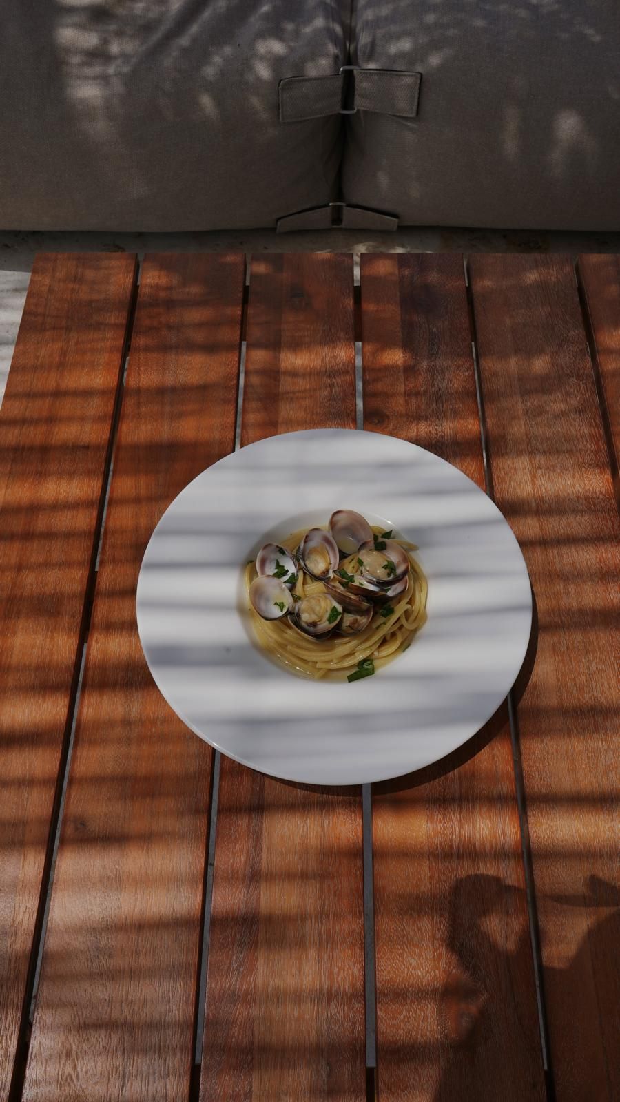 A white plate with pasta and clams on a wooden table.