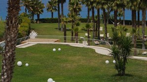 A landscaped area with palm trees, a grassy lawn, and a view of the ocean. - Infinity Resort Tropea (Parghelia)