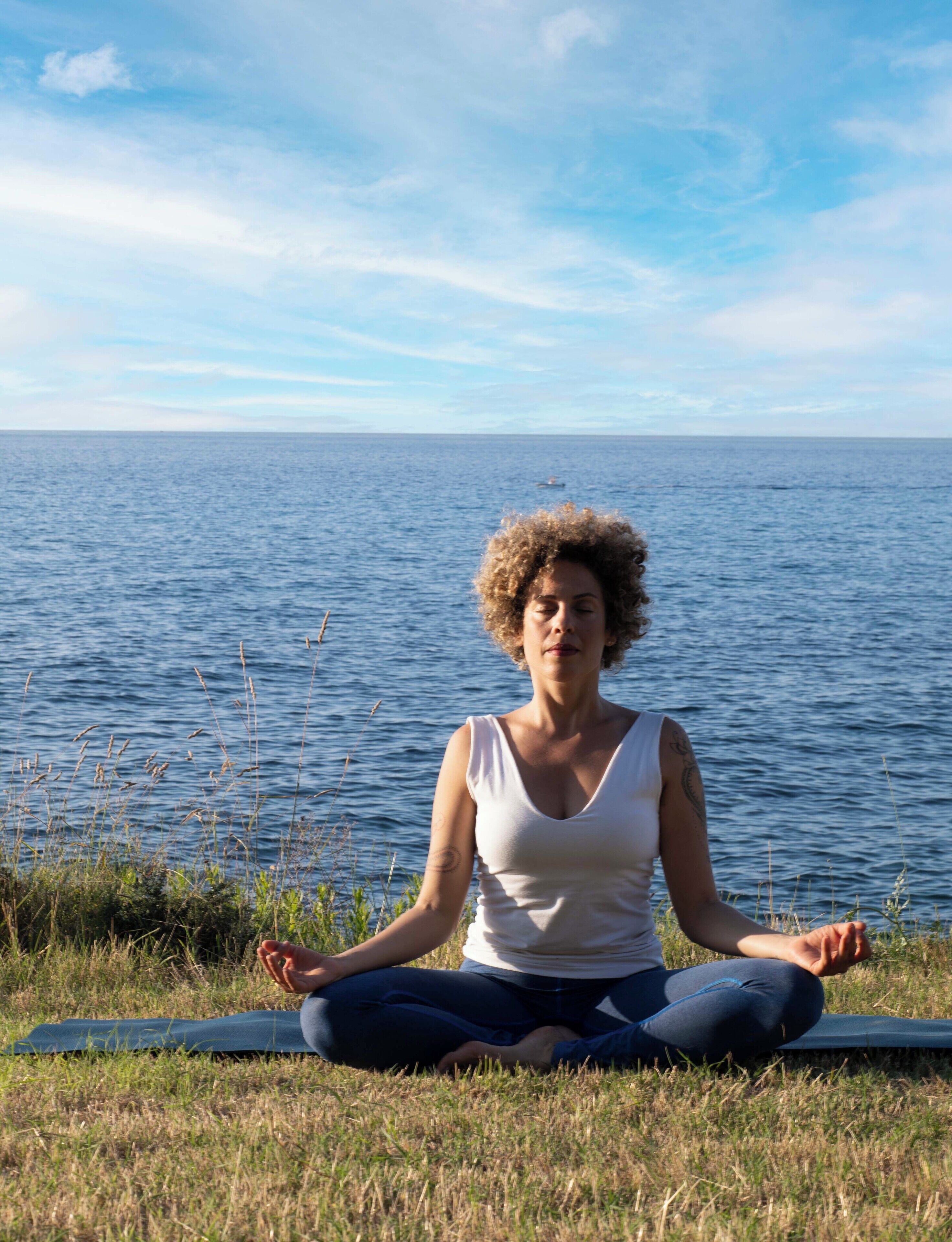 A person meditating on a mat by a body of water.