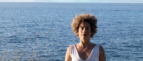 A person meditating on a mat by a body of water.
