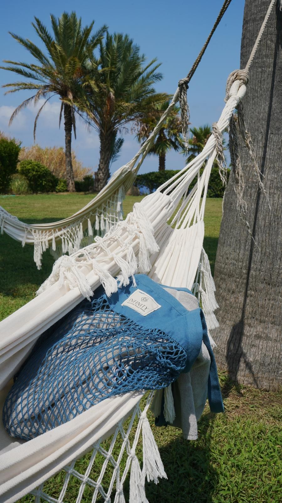 A hammock tied to a tree, with a blue netted bag and a pillow on it.