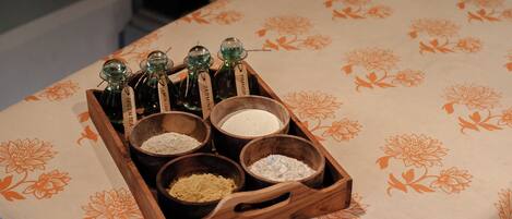 A wooden tray with various spices and a bottle of green tea on a table with a floral tablecloth.