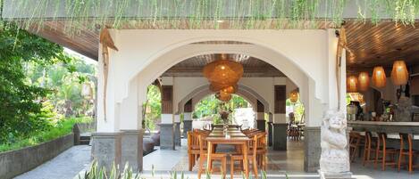 An outdoor dining area with a table and chairs, surrounded by greenery and hanging plants.