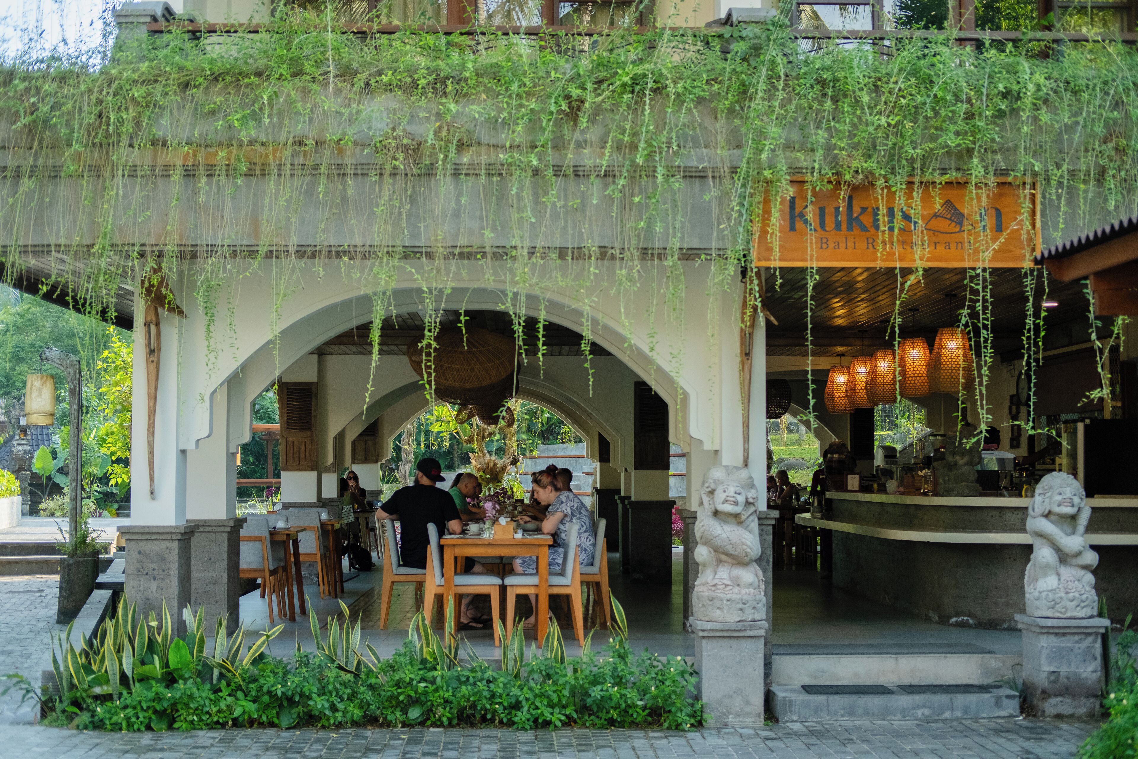 Een restaurant met terras onder een overdekt gedeelte, versierd met hangende planten.