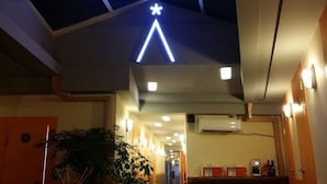 Un couloir d’hôtel avec une enseigne au néon au-dessus, une plante et une machine à café posée sur un comptoir.