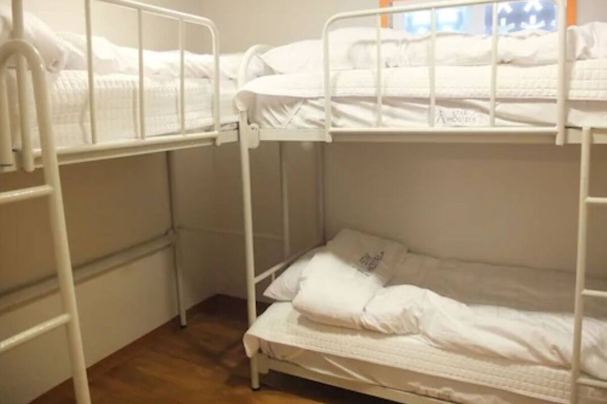 Habitación con literas, una escalera a la izquierda, una ventana con vistas y una colcha blanca.