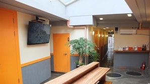 Un couloir d’hôtel moderne avec un banc en bois, une plante en pot et un téléviseur fixé au mur.