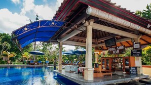 A poolside bar with umbrellas, lounge chairs, and a sign indicating a poolside bar. - Kuta Puri Bungalows, Villas and Resort (Kuta)