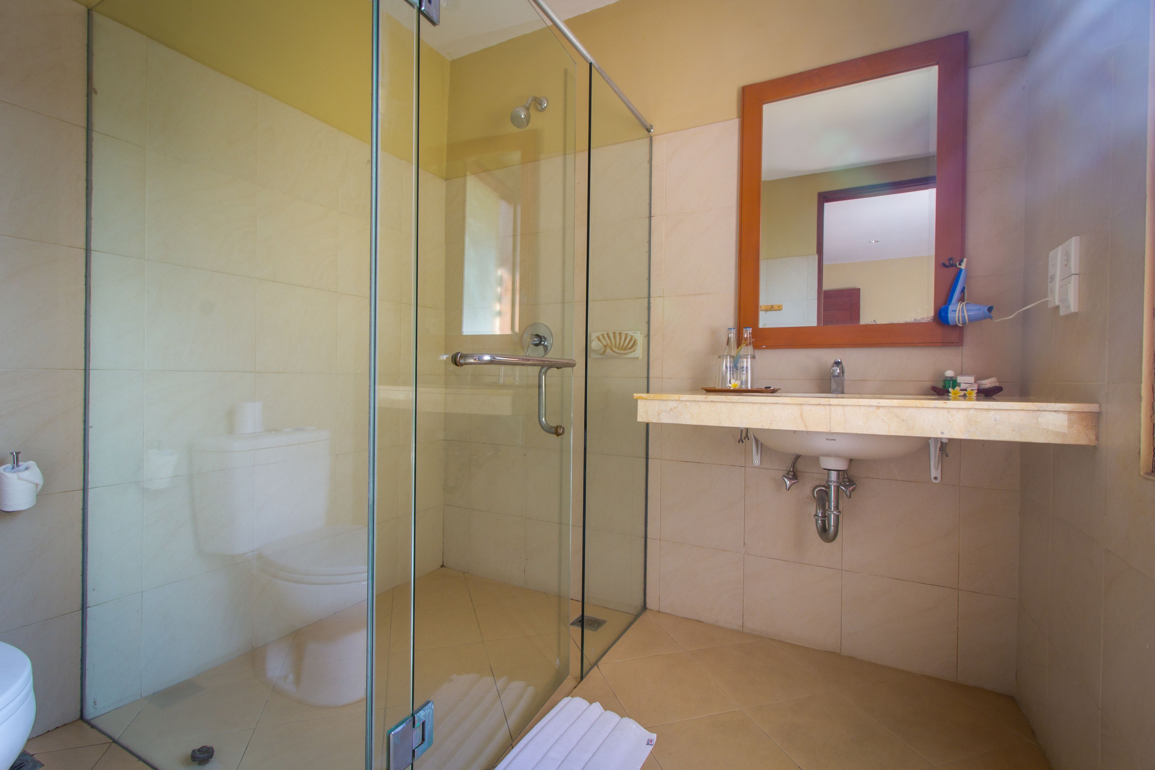 Une salle de bain moderne avec une douche à parois de verre, des toilettes blanches et un lavabo beige avec un miroir au-dessus.
