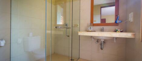 A modern bathroom with a glass-enclosed shower, a white toilet, and a beige sink with a mirror above it.