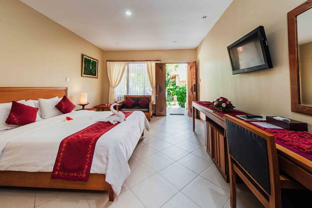 A hotel room with a large bed, a desk with a TV, and a view of the outdoors.