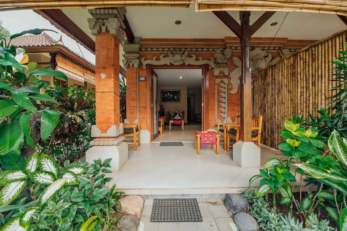 A traditional-style entrance with a covered porch, wooden furniture, and lush greenery.
