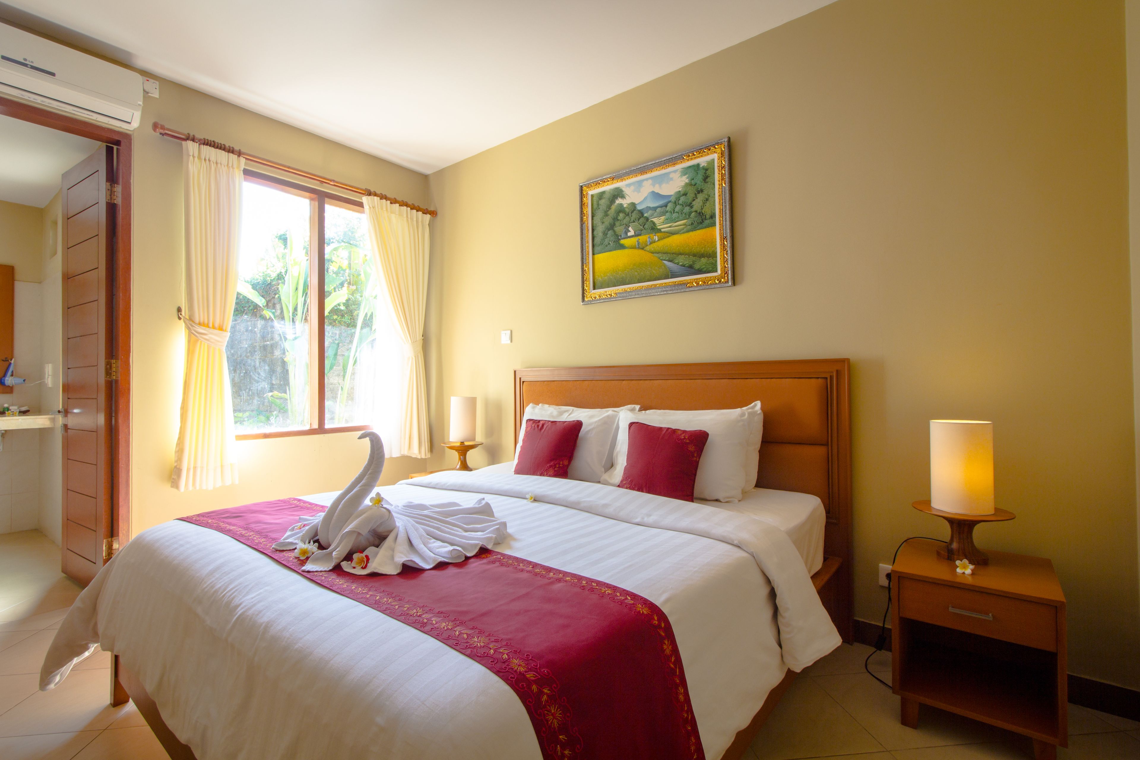 A hotel room with a large bed, a nightstand with a lamp, a painting on the wall, and a window with curtains.