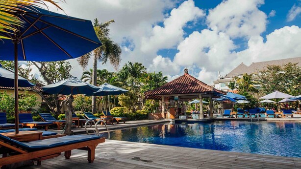 A pool area with lounge chairs and umbrellas, surrounded by palm trees and a gazebo. - Kuta Puri Bungalows, Villas and Resort (Kuta)