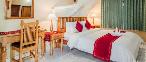 Habitación de hotel con cama de madera, ropa de cama blanca, almohadas rojas, dosel sobre la cama, escritorio con silla, espejo y unidad de aire acondicionado.