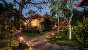A well-lit garden pathway leading to a traditional-style building with a tiled roof, surrounded by lush greenery and decorative lanterns. - Kuta Puri Bungalows, Villas and Resort (Kuta)