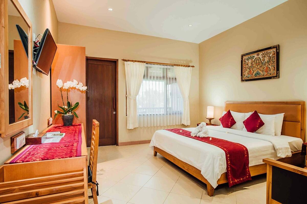 A hotel room with a bed, a desk with a chair, a TV, a window with curtains, and a painting on the wall.