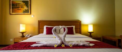 Habitación de hotel con una cama bien hecha, dos lámparas de noche, un cuadro en la pared y un cabecero de madera.