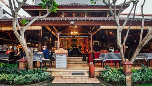 An outdoor restaurant with checkered tablecloths, wooden pillars, and a covered seating area. - Kuta Puri Bungalows, Villas and Resort (Kuta)