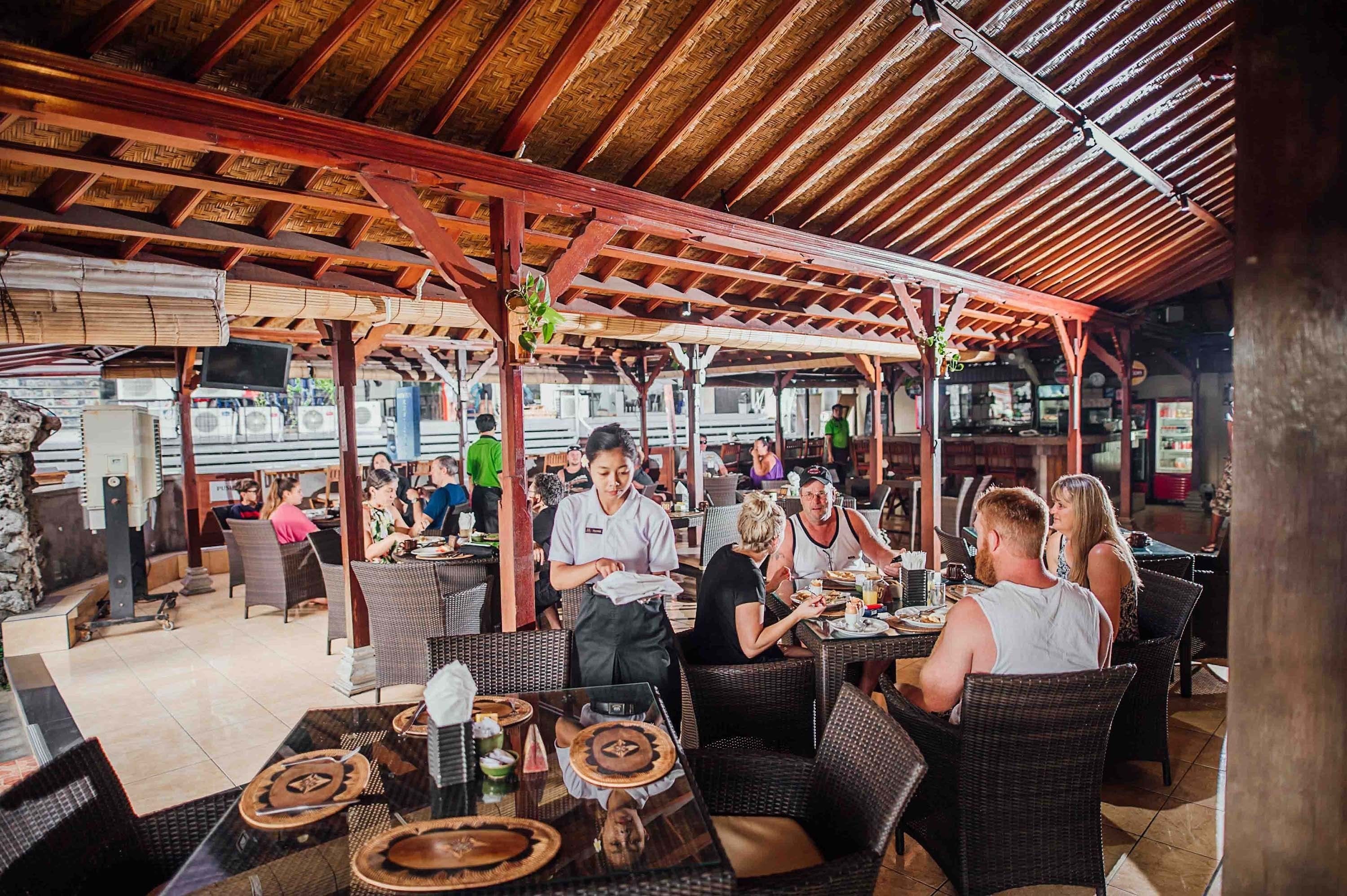 An outdoor restaurant with wicker furniture and a wooden ceiling.